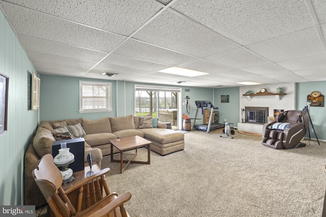 living area featuring carpet floors, a paneled ceiling, and a glass covered fireplace