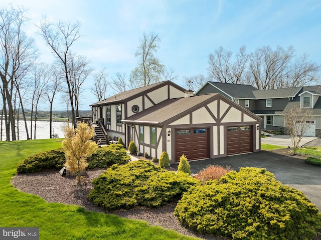 view of front facade with stucco siding, a garage, a front lawn, aphalt driveway, and a water view