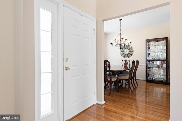 entrance foyer featuring light wood finished floors, a notable chandelier, a wealth of natural light, and baseboards