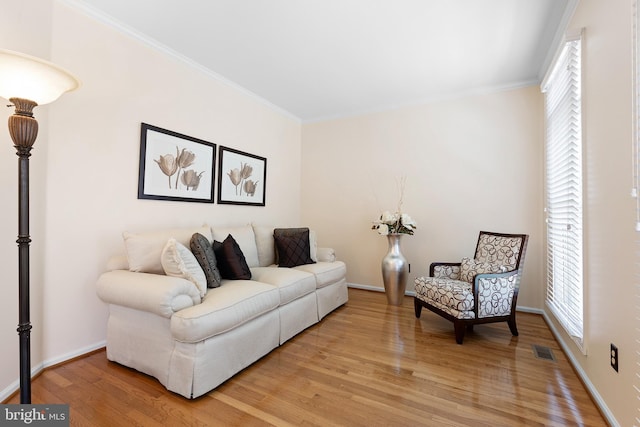 living room with visible vents, light wood-type flooring, ornamental molding, and baseboards