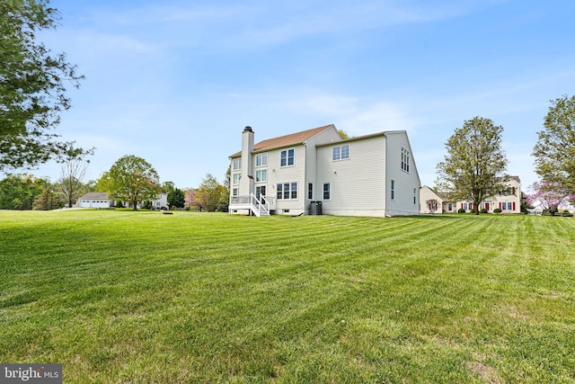rear view of house with cooling unit, a chimney, and a yard