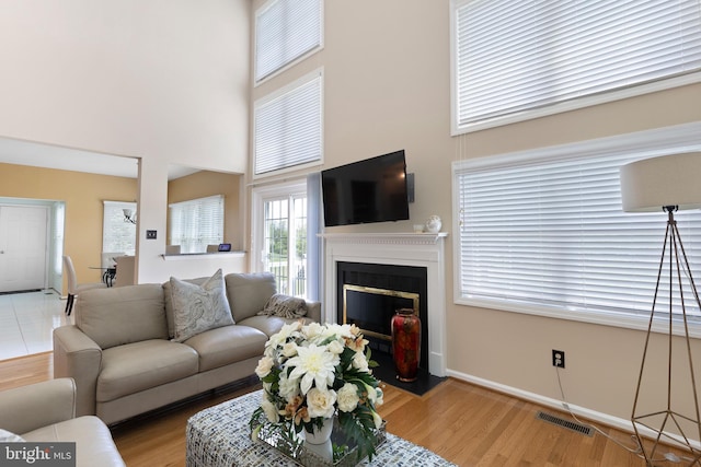 living area with a fireplace with flush hearth, visible vents, baseboards, a towering ceiling, and wood finished floors