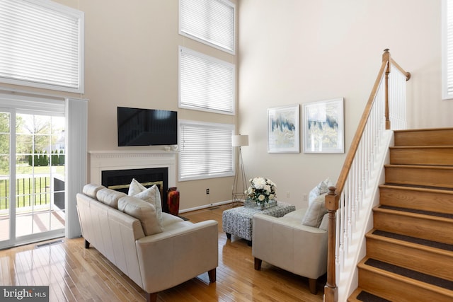 living room featuring visible vents, light wood-type flooring, a fireplace, a towering ceiling, and stairs