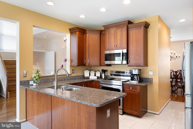 kitchen with dark stone counters, brown cabinetry, stainless steel appliances, a sink, and a peninsula