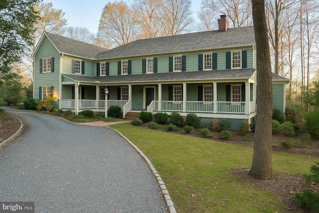 colonial home featuring a front lawn, a chimney, covered porch, and roof with shingles