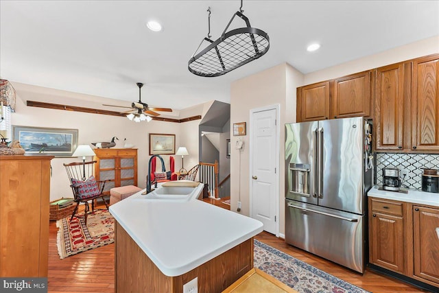 kitchen with a kitchen island, light countertops, backsplash, a sink, and stainless steel refrigerator with ice dispenser