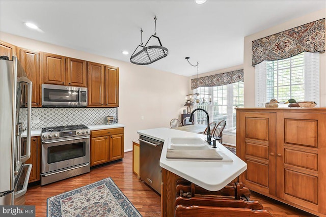 kitchen featuring a sink, stainless steel appliances, light countertops, a kitchen island with sink, and brown cabinetry