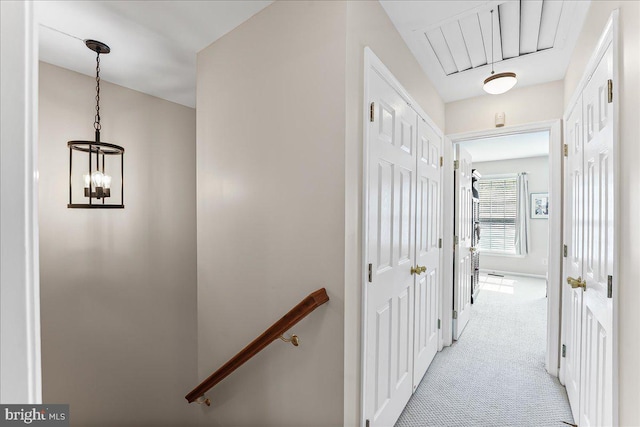 corridor with attic access, an upstairs landing, a chandelier, and light carpet
