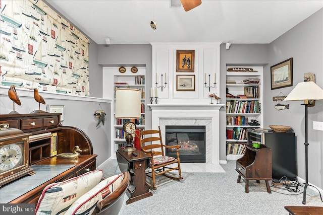 living area featuring baseboards, a ceiling fan, a premium fireplace, and carpet flooring