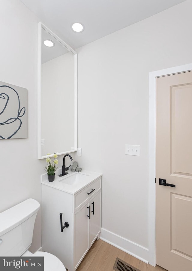 half bath featuring wood finished floors, vanity, baseboards, toilet, and visible vents