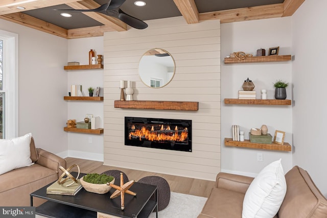 living room featuring beam ceiling, baseboards, wood finished floors, a large fireplace, and ceiling fan