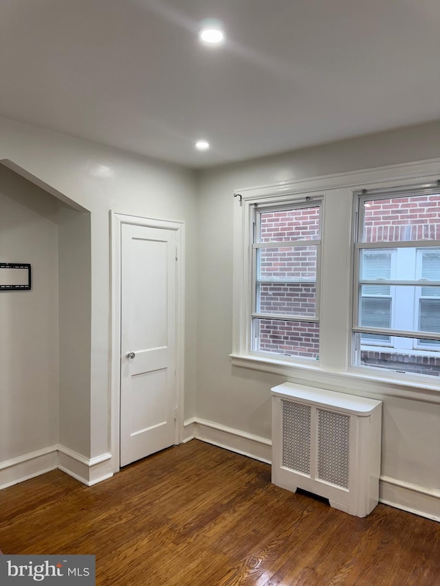 unfurnished room with wood finished floors, baseboards, recessed lighting, and radiator