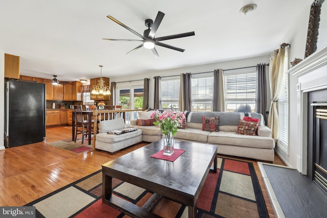 living area with ceiling fan with notable chandelier and light wood-style flooring