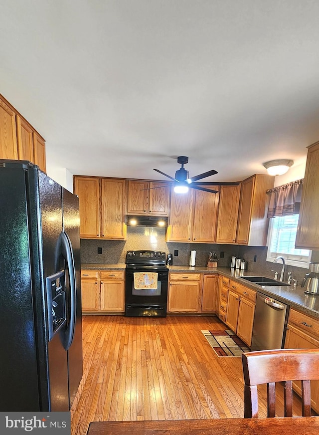 kitchen with backsplash, a sink, black appliances, light wood-style floors, and under cabinet range hood