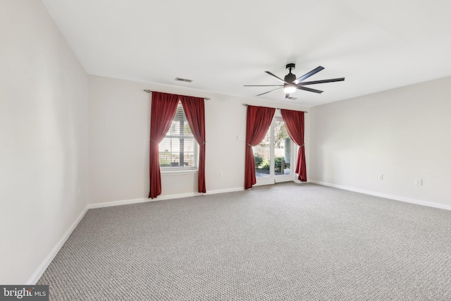 carpeted empty room with baseboards, a ceiling fan, and visible vents