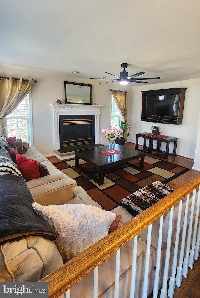 living room featuring a fireplace with raised hearth and ceiling fan