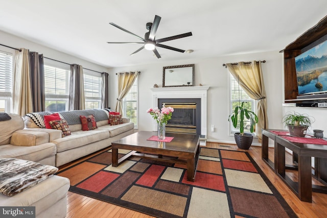 living room with plenty of natural light, ceiling fan, wood-type flooring, and a glass covered fireplace