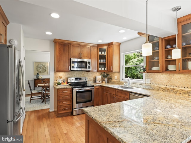 kitchen with light stone counters, brown cabinetry, light wood-style floors, appliances with stainless steel finishes, and a sink