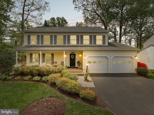 colonial home featuring driveway, covered porch, and a lawn