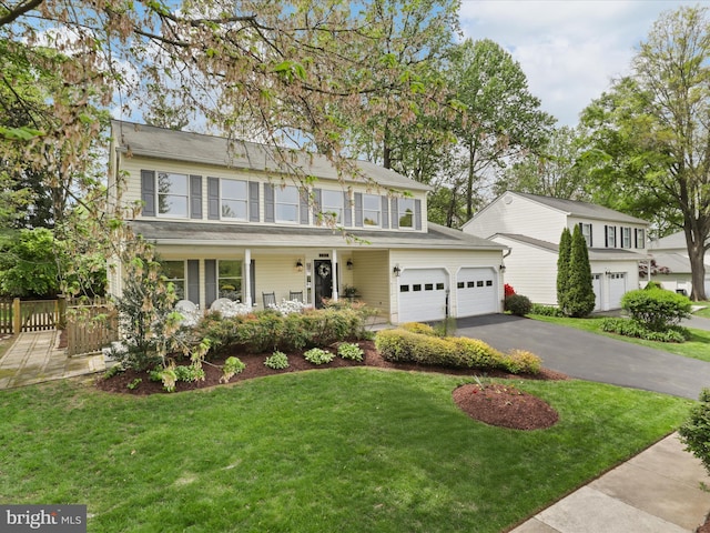 colonial house with driveway, fence, covered porch, and a front yard