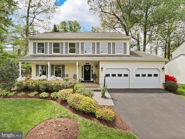 colonial house featuring driveway, a front yard, and a porch