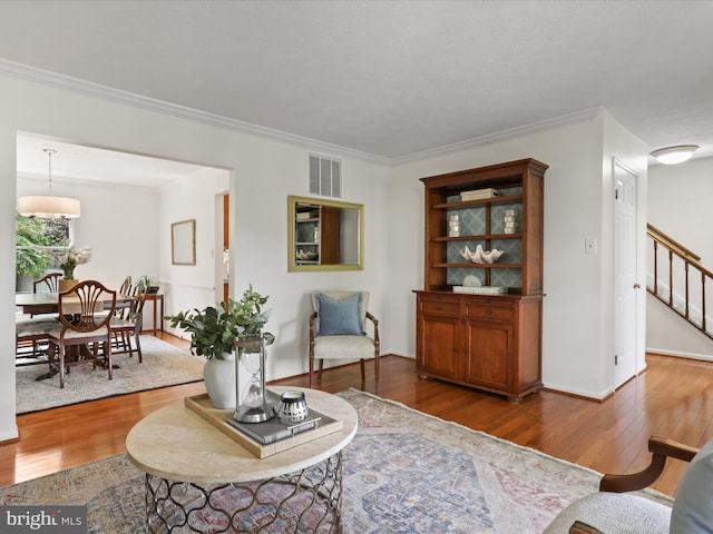 living area with crown molding, stairway, visible vents, baseboards, and wood finished floors