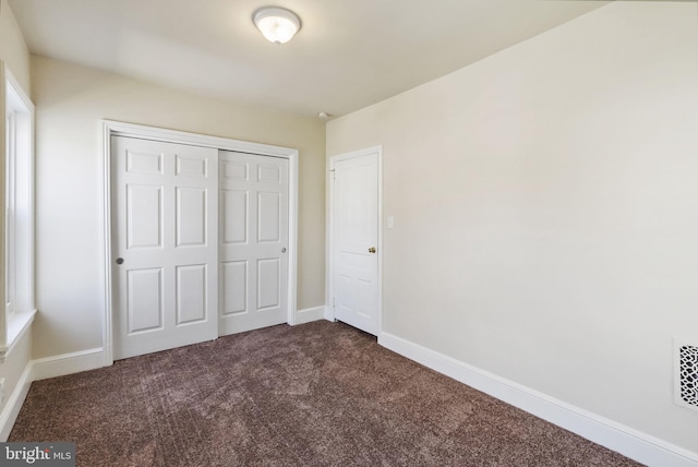 unfurnished bedroom featuring baseboards, dark colored carpet, and a closet