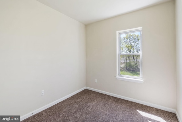 empty room with dark carpet, baseboards, and plenty of natural light