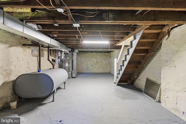 unfinished basement featuring heating fuel, heating unit, and stairway