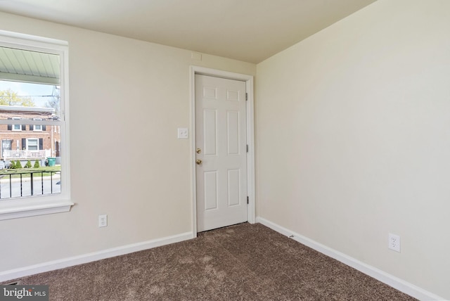 empty room featuring dark colored carpet and baseboards