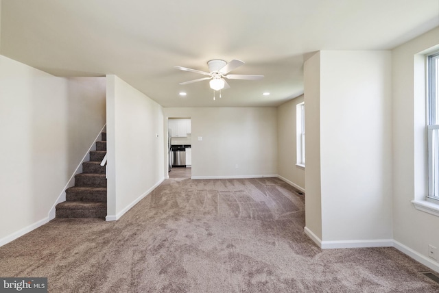 unfurnished living room with ceiling fan, stairway, light colored carpet, and a healthy amount of sunlight