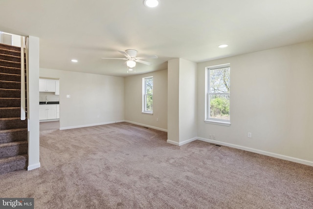unfurnished living room with light carpet, a ceiling fan, a wealth of natural light, and stairs