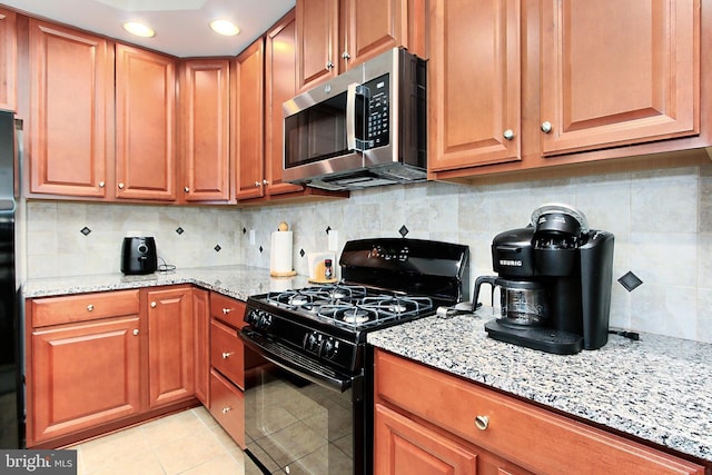 kitchen featuring black range with gas stovetop, light stone counters, decorative backsplash, light tile patterned flooring, and stainless steel microwave