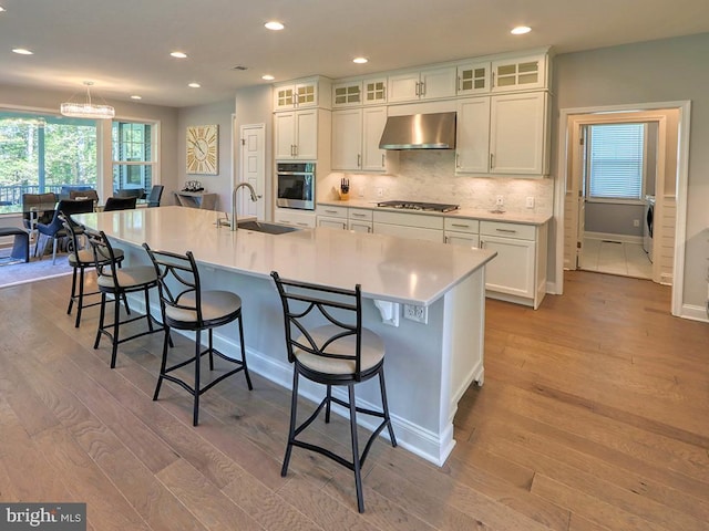 kitchen with ventilation hood, stainless steel appliances, a sink, light wood-type flooring, and white cabinets