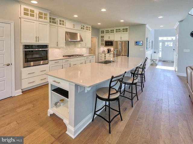 22144 Welches Way, Lewes, DE 19958 - kitchen with appliances with stainless steel finishes, a sink, wall chimney range hood, light wood-style floors, and white cabinets