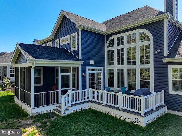 rear view of house with a sunroom, a shingled roof, a lawn, and a wooden deck