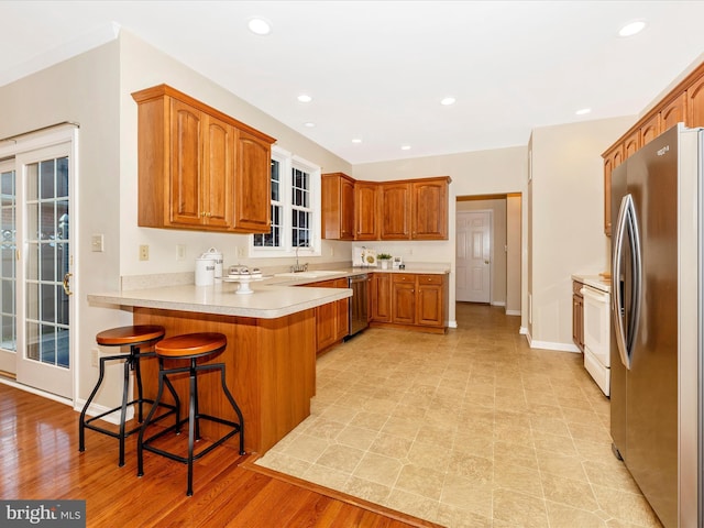 kitchen with a peninsula, brown cabinetry, appliances with stainless steel finishes, and a breakfast bar