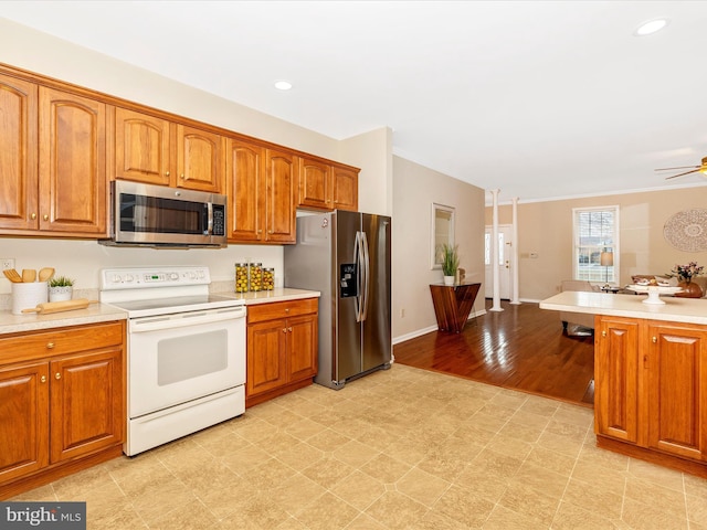 kitchen with stainless steel appliances, brown cabinets, ceiling fan, light countertops, and ornamental molding