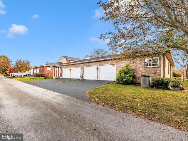 view of front of house featuring central air condition unit, brick siding, an attached garage, a front yard, and aphalt driveway