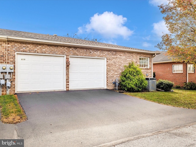 exterior space with central AC unit, driveway, an attached garage, brick siding, and roof with shingles