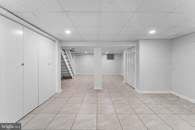finished below grade area featuring stairway, a drop ceiling, light tile patterned flooring, recessed lighting, and baseboards