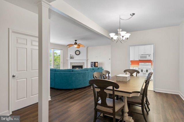 dining room featuring dark wood-style flooring, baseboards, a lit fireplace, and ceiling fan with notable chandelier