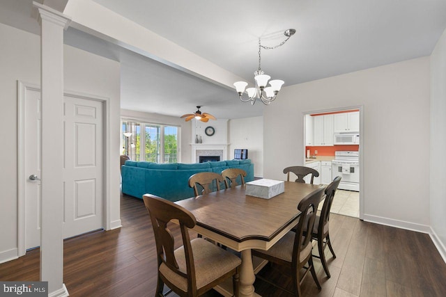 dining area with baseboards, a fireplace, ceiling fan with notable chandelier, and dark wood-style flooring