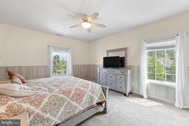 bedroom with wooden walls, ceiling fan, light colored carpet, and wainscoting