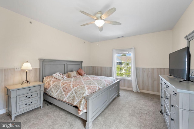 bedroom featuring wood walls, wainscoting, a ceiling fan, and light carpet