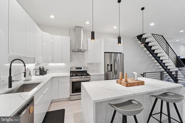 kitchen with stainless steel appliances, wall chimney range hood, modern cabinets, a sink, and white cabinetry