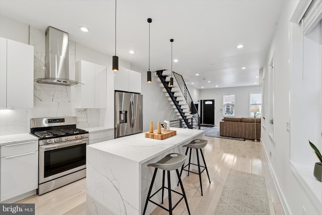 kitchen featuring stainless steel appliances, wall chimney range hood, a breakfast bar area, a kitchen island, and white cabinets