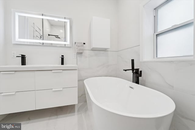 bathroom with double vanity, a freestanding tub, and tile walls