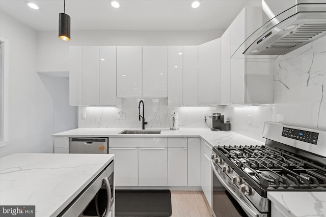 kitchen with appliances with stainless steel finishes, wall chimney exhaust hood, a sink, modern cabinets, and white cabinetry