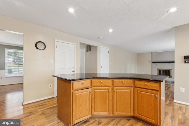 15915 Marlington Dr, Dumfries, VA 22025 - kitchen featuring light wood finished floors, a textured ceiling, baseboards, a brick fireplace, and a center island